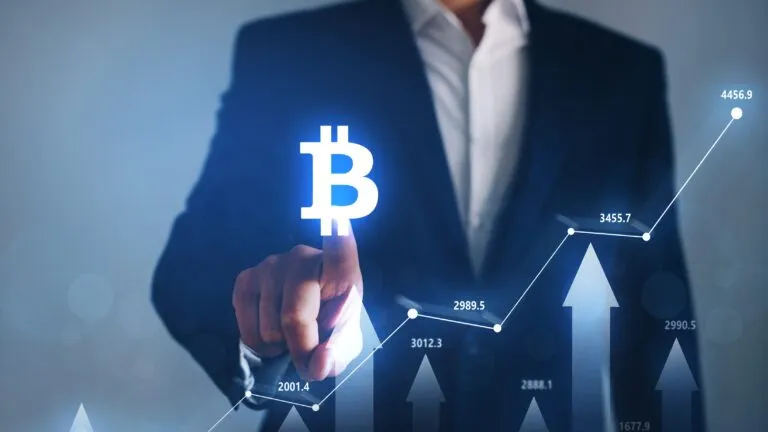 Hombre de negocios tocando el símbolo de Bitcoin con gráfico ascendente, reflejando el alza a más de 64 mil dólares tras señales de la Fed sobre posibles recortes de tasas.