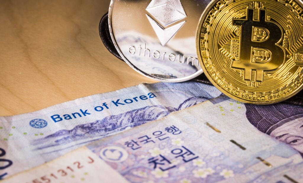 Monedas de Bitcoin y Ethereum sobre billetes del Banco de Corea, reflejando la regulación cripto y stablecoins respaldadas por el won en Corea del Sur