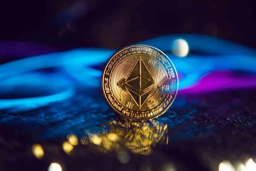 Moneda física de Ethereum sobre una superficie oscura iluminada por luces azul y púrpura, simbolizando impulso del mercado y confianza en el precio de ETH.