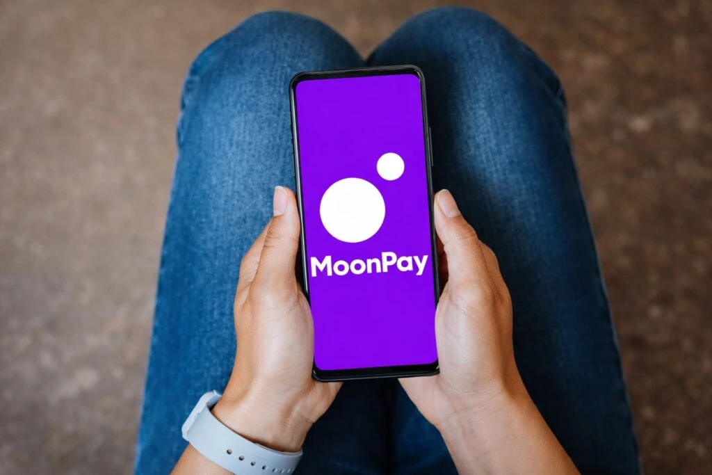 Manos sosteniendo móvil con MoonPay rampa cripto en pantalla para pagos autónomos con IA